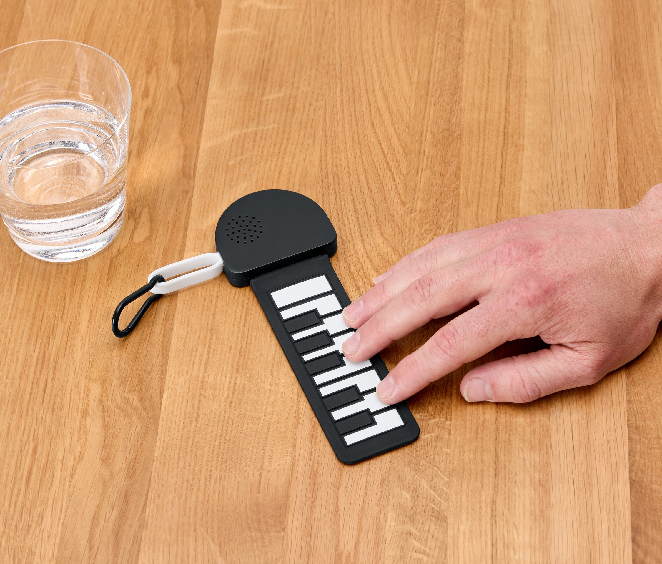 Eine Hand spielt auf einem Mini-Klavier neben einem Glas Wasser.