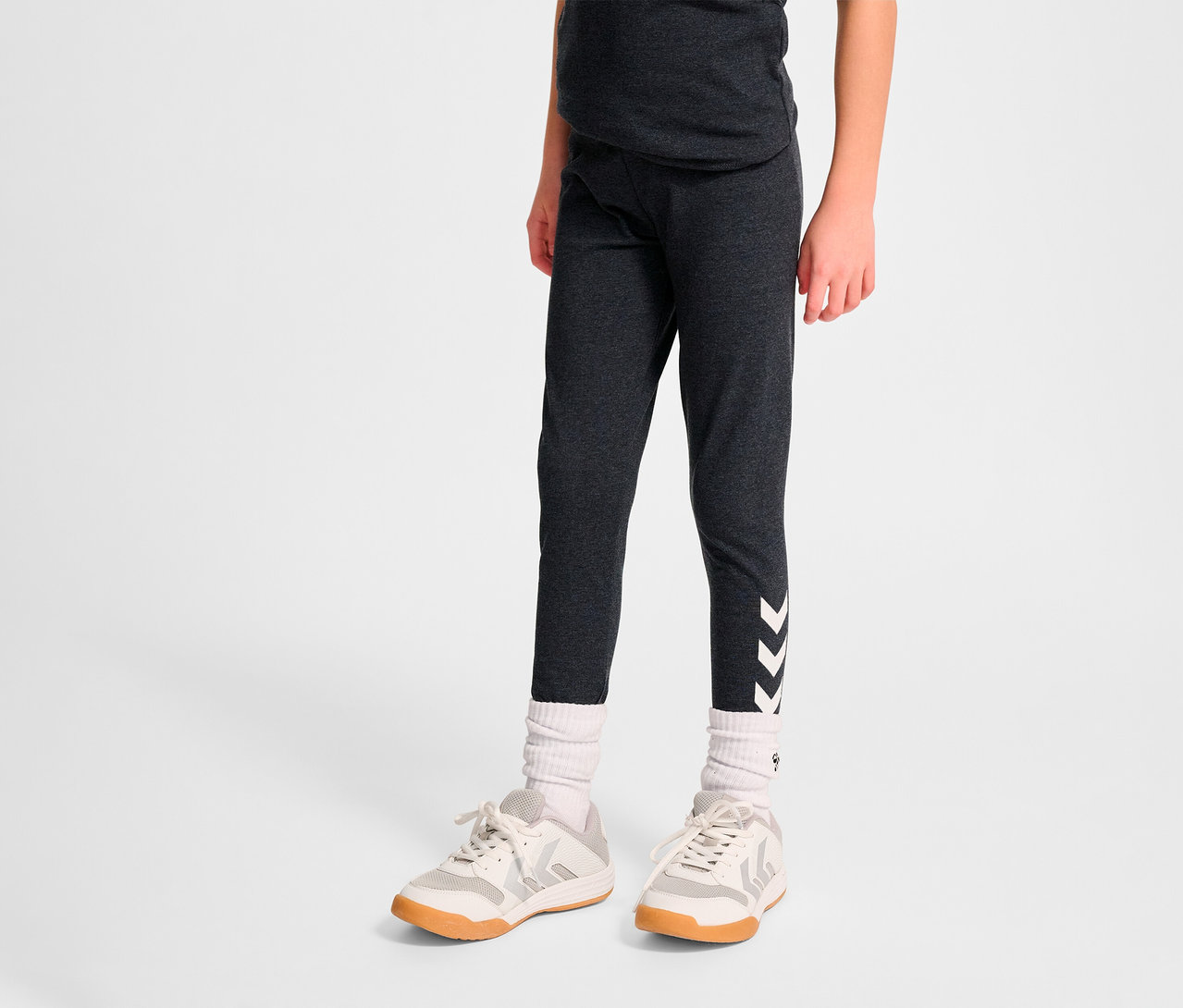 Person trägt dunkle HUMMEL HMLJR Logo Tight Leggings mit weißen Winkeln am Bein.
