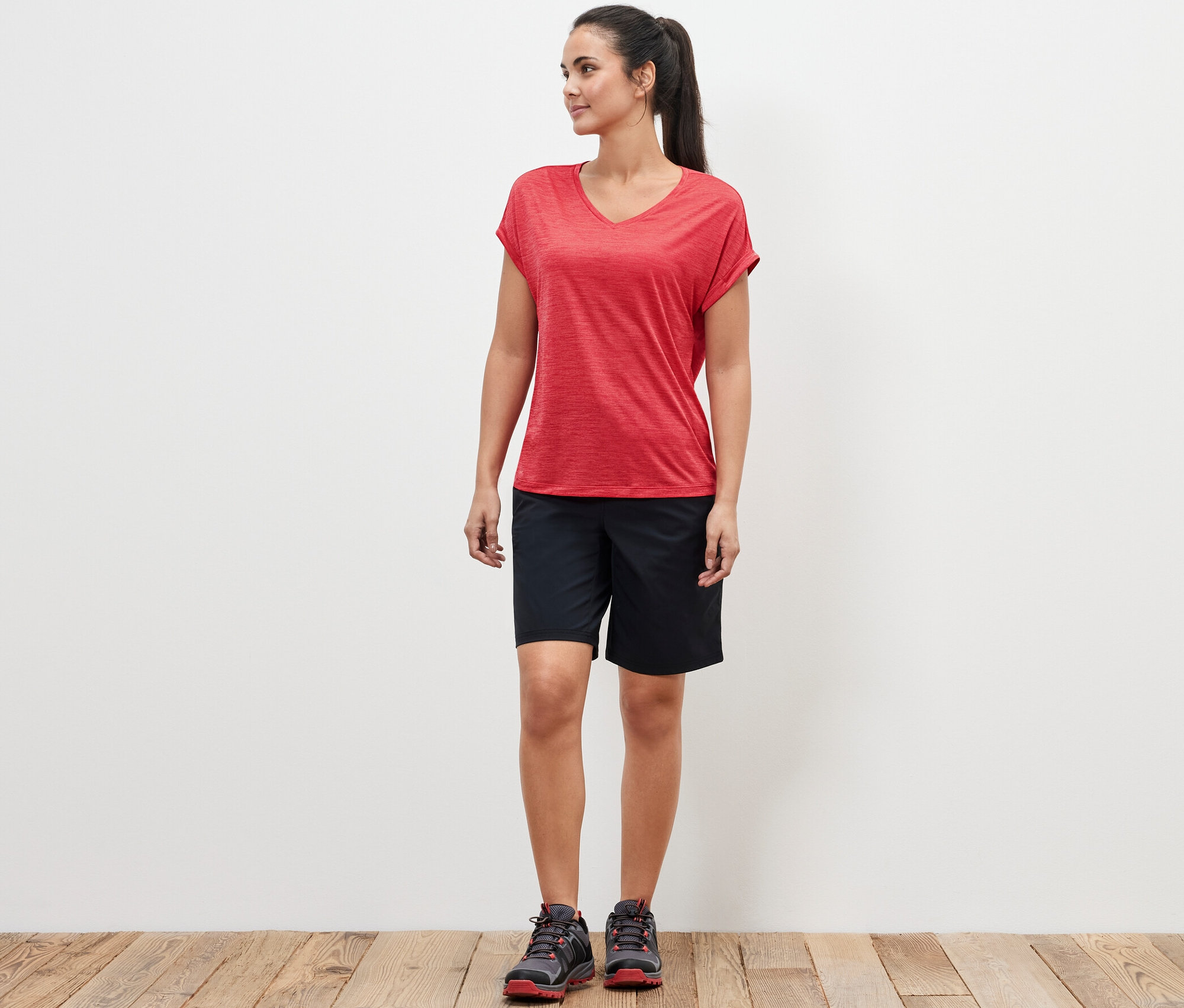 Eine Frau steht und trägt ein pinkes Funktionsshirt und schwarze Shorts.