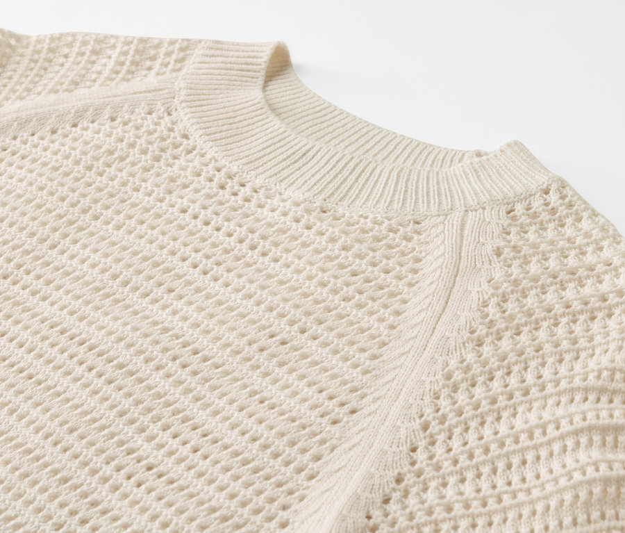 Detailaufnahme eines Pullovers in Pointellestrick auf weißem Hintergrund.