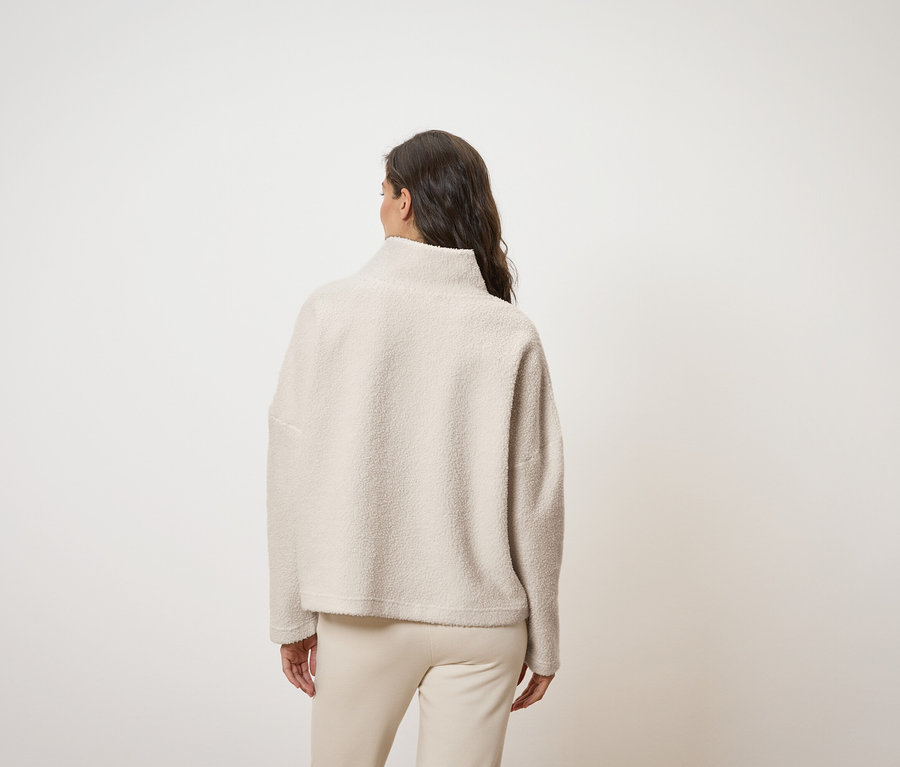 Eine von hinten gezeigte Frau trägt ein cremefarbenes Oberteil mit hohem Kragen und cremefarbene Hosen.