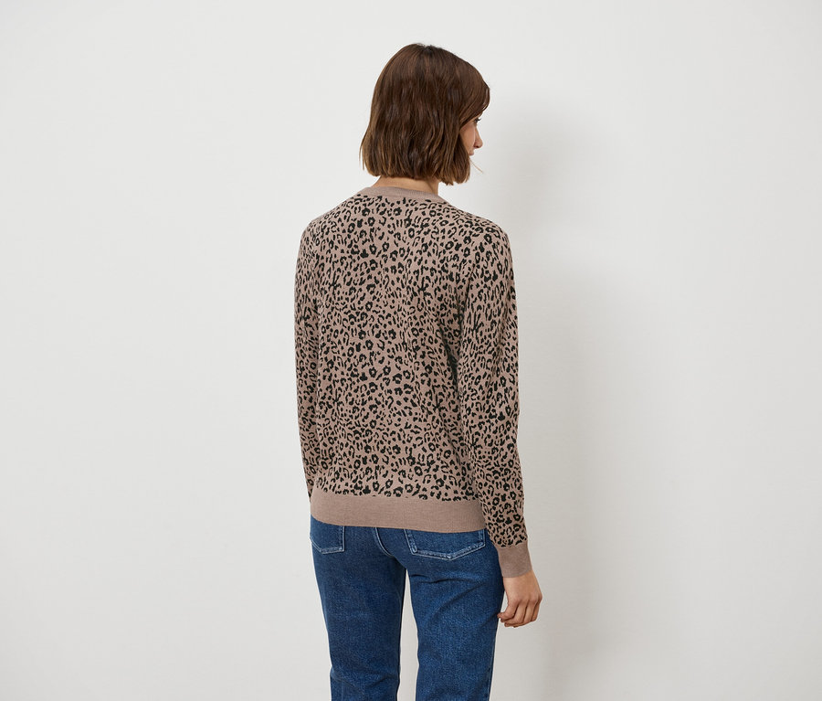 Rückansicht einer Frau mit kurzem braunem Haar in einer braunen Bluse mit Tiermuster und blauen Jeans.