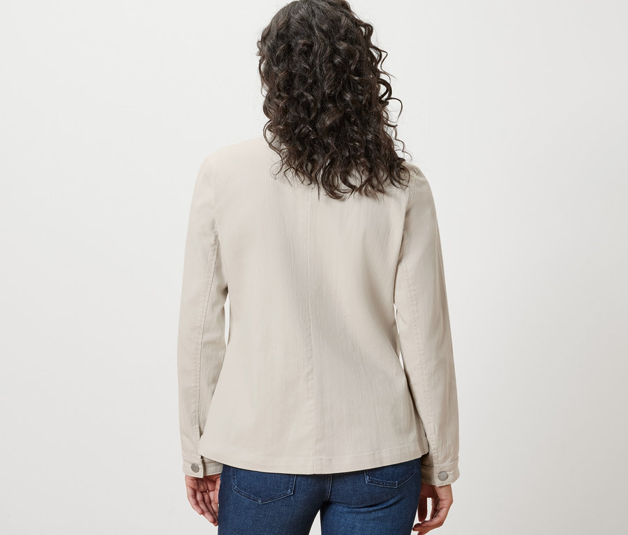 Rückansicht einer Frau mit braunem, gewelltem Haar, die eine Jeansjacke mit Cargotaschen und blaue Jeans trägt.