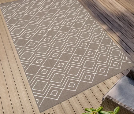 Ein brauner, faltbarer Outdoor-Teppich »Diamond Rhythm« mit weißem geometrischen Muster liegt auf einer Holzterrasse.