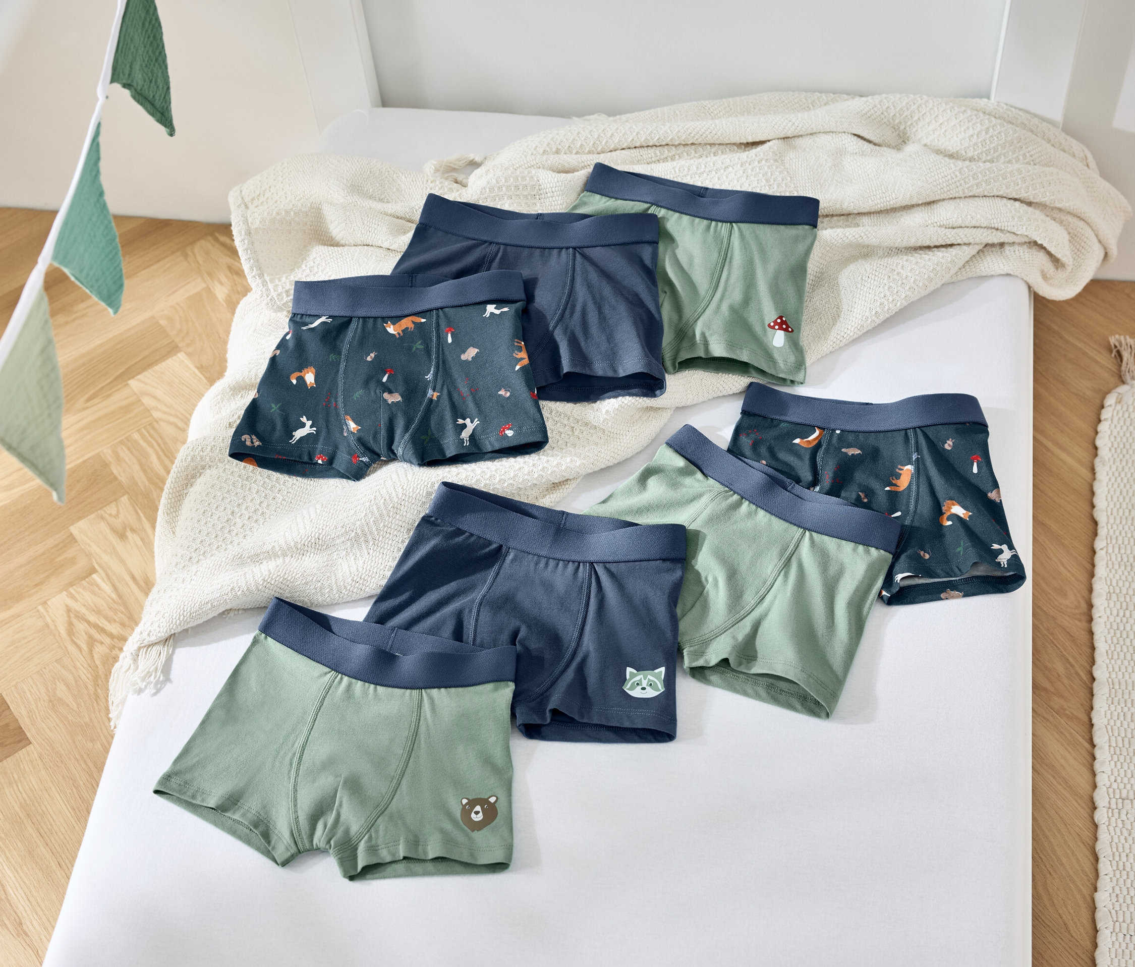 Sechs Jungen-Boxershorts liegen auf einem weißen Bett mit einer beigen Decke.