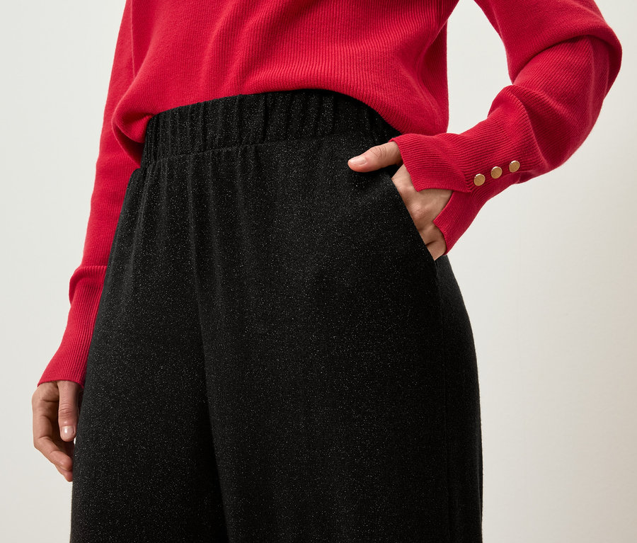 Detailaufnahme einer Frau im roten Pullover mit der Hand in der Tasche einer schwarzen Glitzerhose.