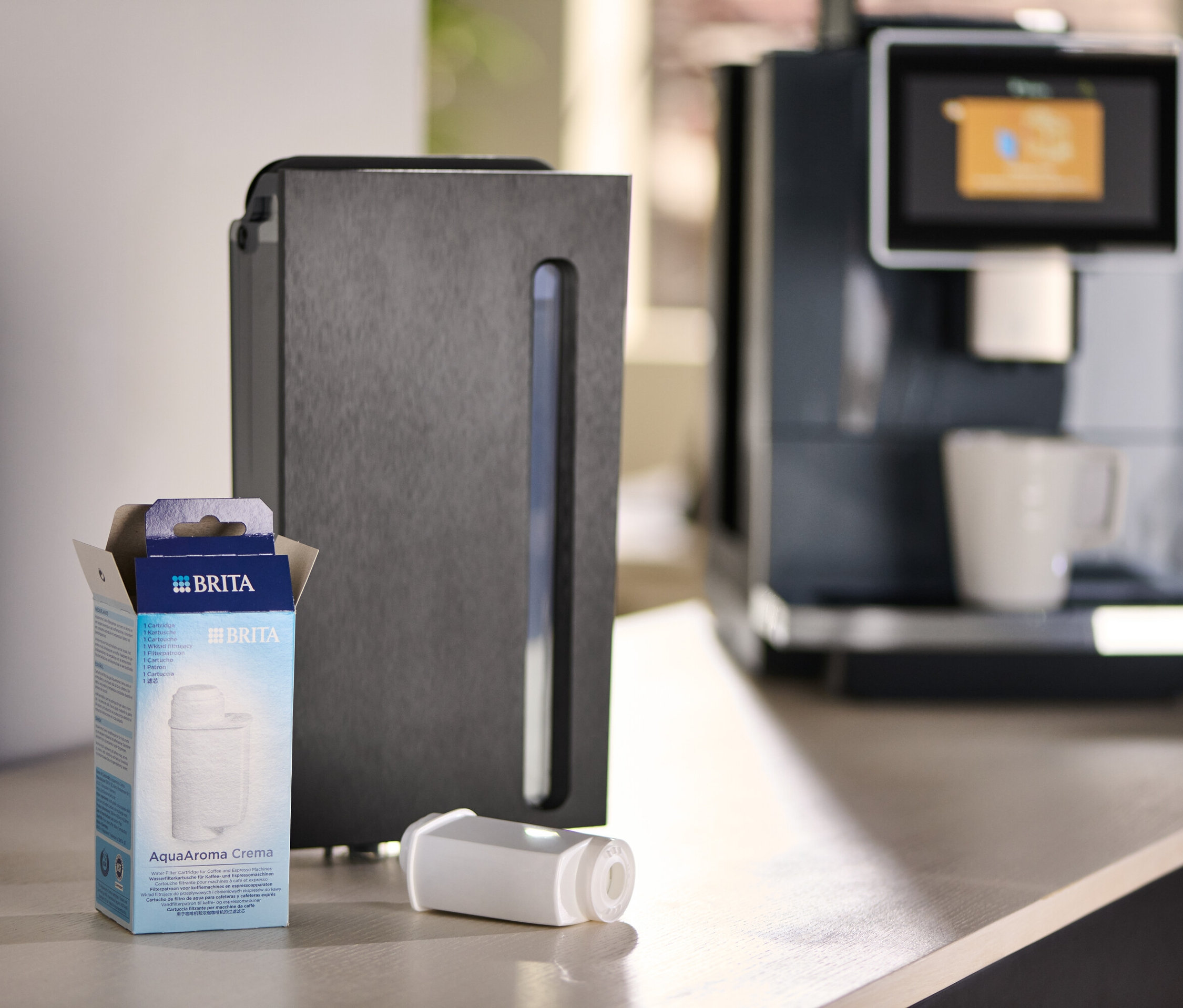 Eine Packung Brita AquaAroma Crema Filter neben einem Filter und einer Kaffeemaschine.