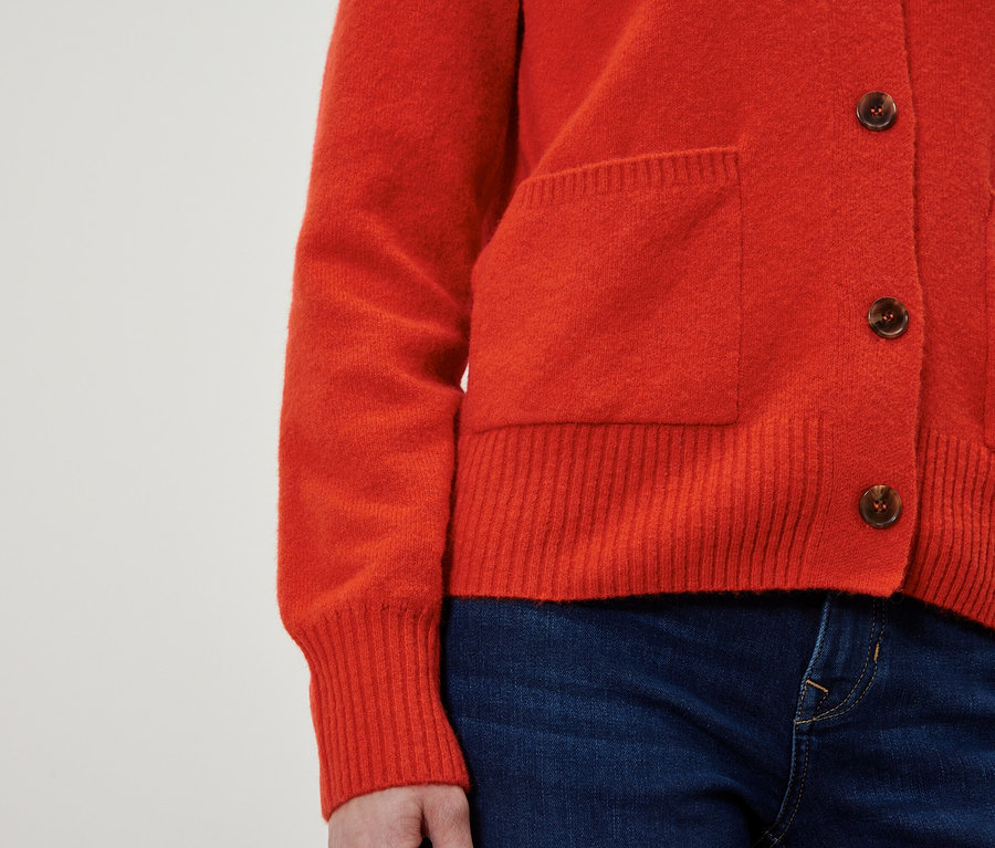 Roter Cardigan mit braunen Knöpfen und blauen Jeans.