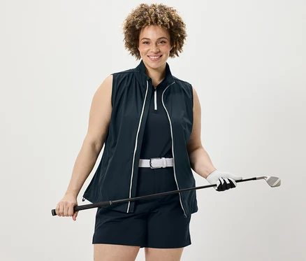 Frau hält Golfschläger, trägt dunkelblaues Funktionstop, Softshell-Funktionsshorts und Softshellweste.