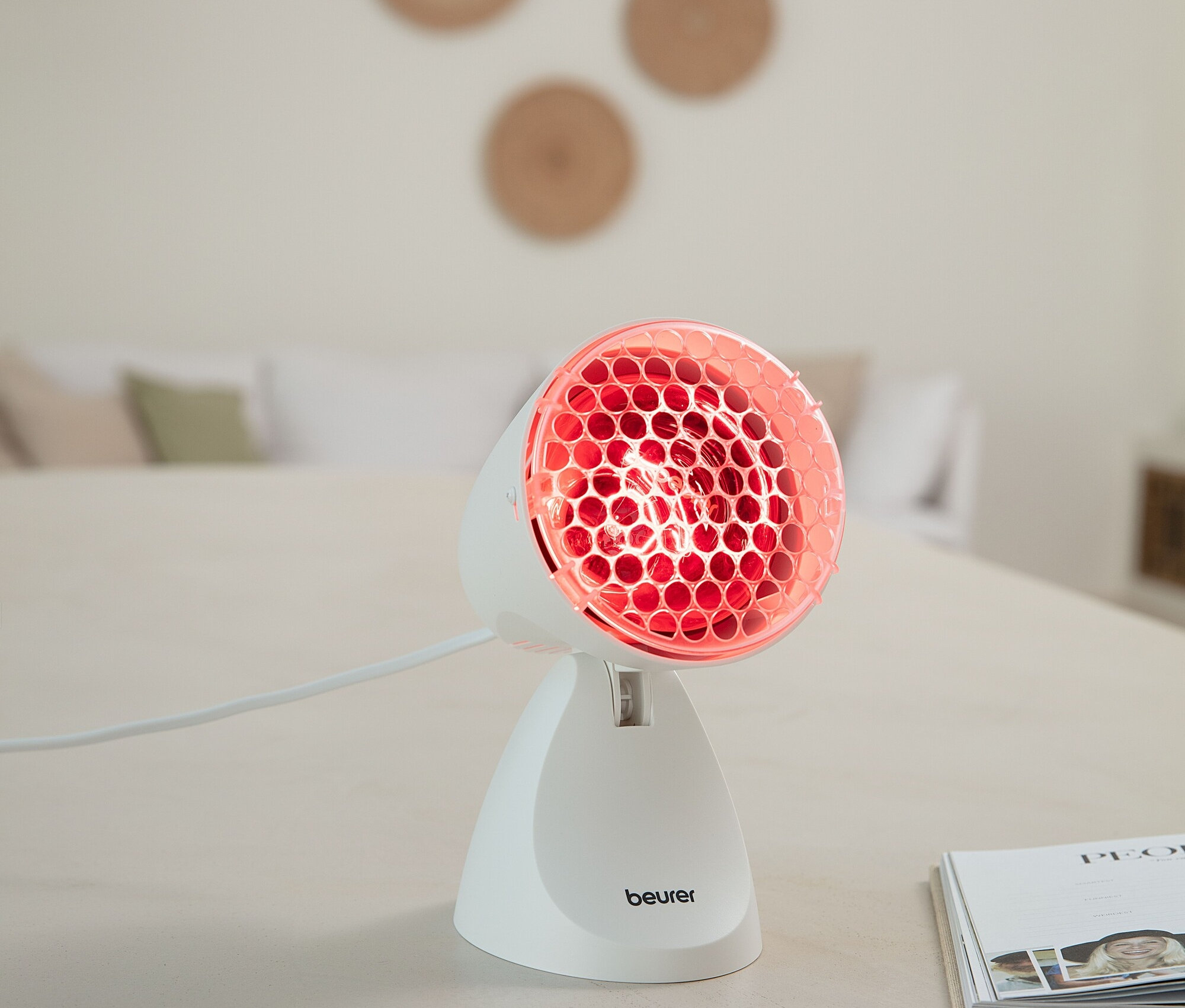 Eine Beurer Infrarotlampe steht auf einem Tisch und strahlt rotes Licht aus.
