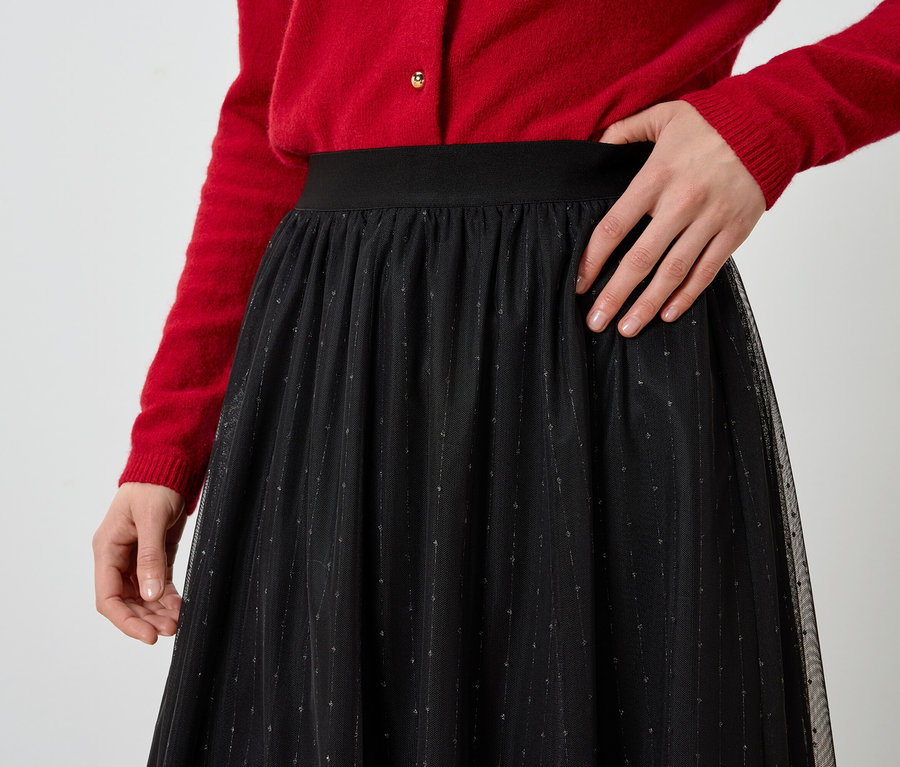 Teilansicht einer Frau in rotem Cardigan und schwarzem Rock.