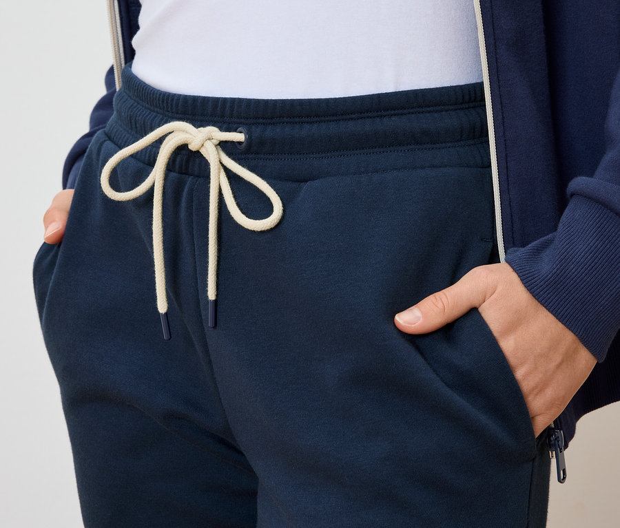 Person mit Händen in den Taschen einer dunkelblauen Jogginghose mit hellem Kordelzug.