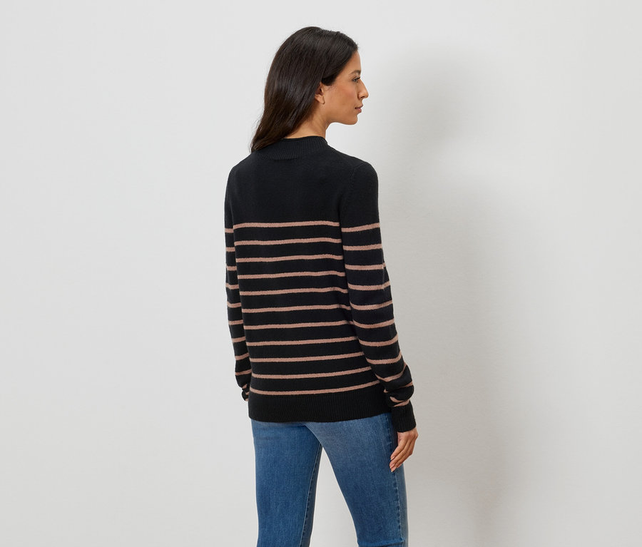Rückansicht einer Frau mit dunklen, schulterlangen Haaren, die einen schwarzen Rollkragenpullover mit horizontalen braunen Streifen und blaue Jeans trägt.
