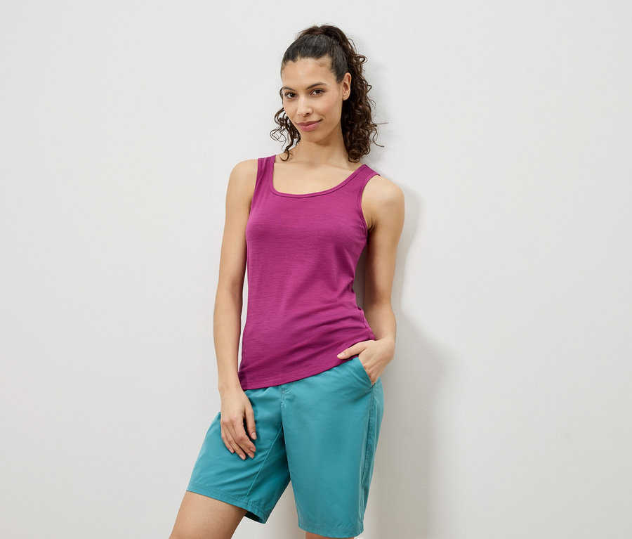Frau posiert in einem pinken Tanktop und türkisfarbenen Shorts vor einer weißen Wand.