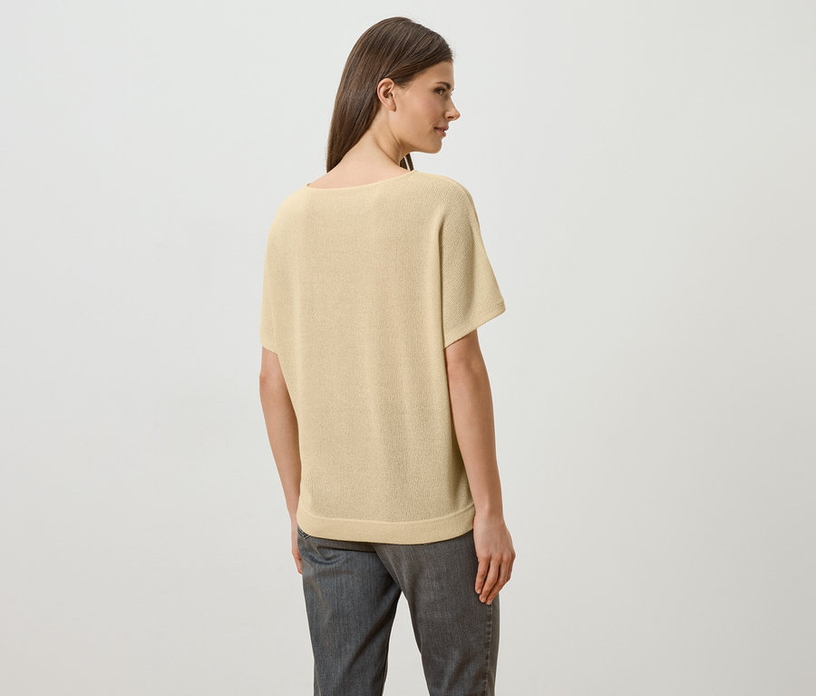 Eine Frau mit langen braunen Haaren trägt ein hellgelbes T-Shirt und graue Jeans, von hinten gesehen.