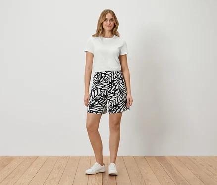 Frau steht in weißem T-Shirt und gemusterten Shorts.