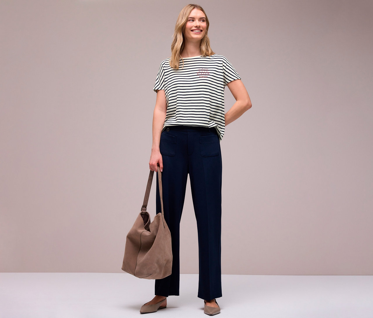 Frau in marineblauer Hose mit Tasche und navy-weißem Street One T-Shirt mit Streifen und Schriftzug, hält eine Tasche.