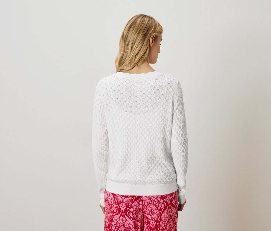 Rückansicht einer blonden Frau mit weißem Strickpullover und rosafarbener Hose mit Muster.