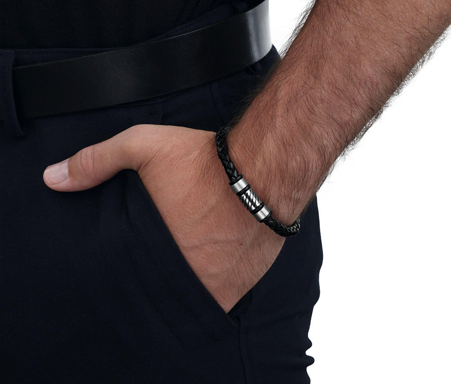 Nahaufnahme von einem Mann, der eine schwarze, geflochtene Armband mit silbernen Akzenten trägt, während seine Hand in einer dunklen Hose steckt.