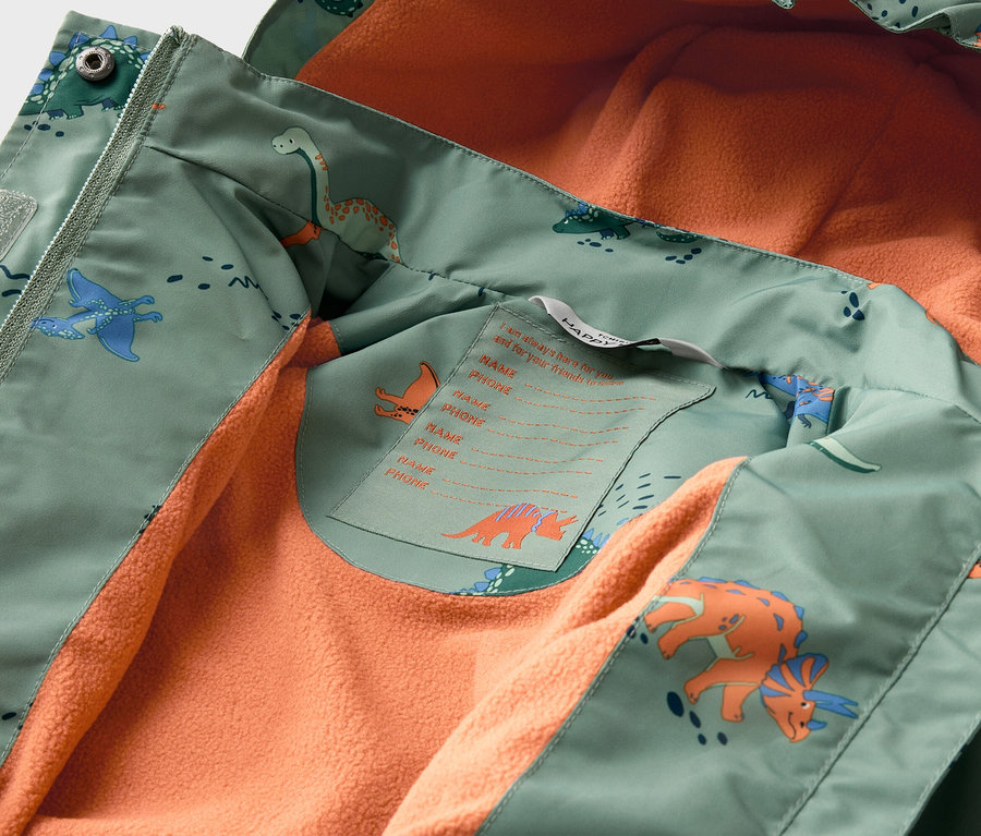 Innenansicht einer geöffneten, hellgrünen Jacke mit Dinosaurier-Muster und orangefarbenem Fleecefutter.