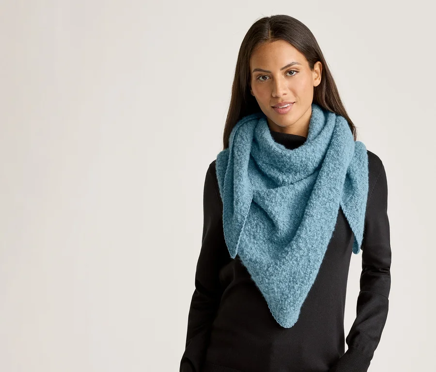 Frau mit langen, dunklen Haaren trägt einen hellblauen, dreieckigen Schal und einen schwarzen Pullover vor einem hellen Hintergrund.