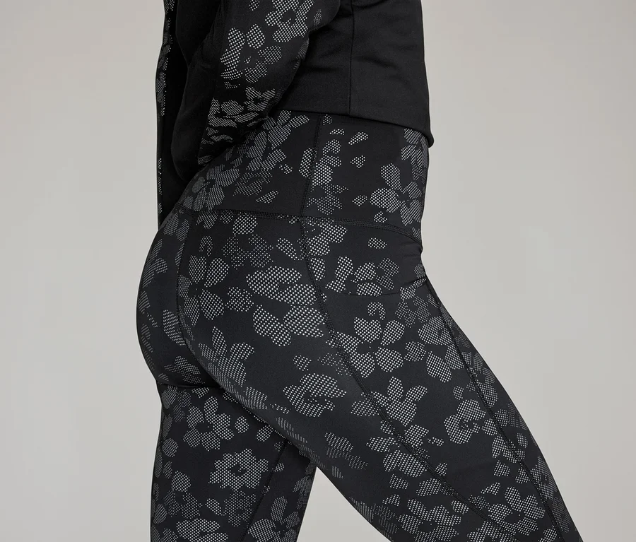 Nahaufnahme einer Frau in Leggings und Oberteil mit Blumenmuster vor grauem Hintergrund.