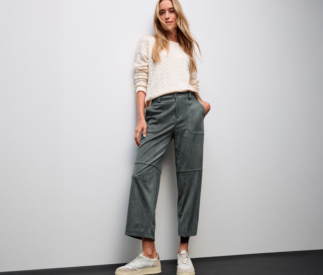 Frau posiert in cremefarbenem Pullover und grüner Street One Velourshose Straight Leg und weißen Turnschuhen.