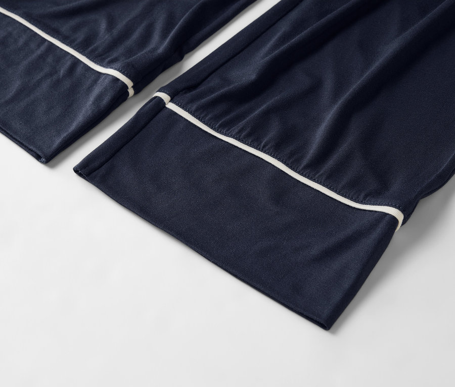 Nahaufnahme von marineblauen Pyjamahosen mit weißer Paspelierung auf weißem Hintergrund.