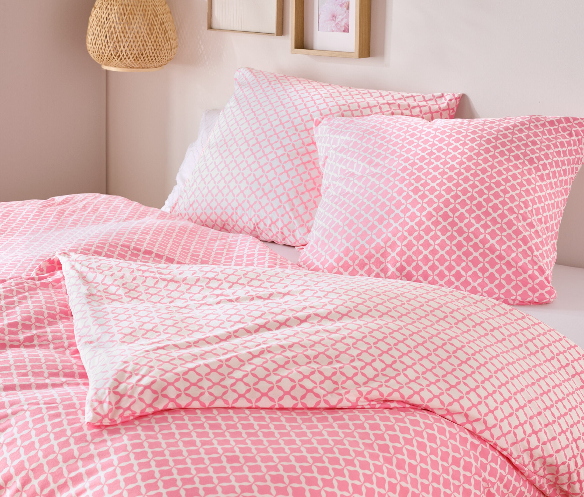 Nahaufnahme von einem Bett mit rosa-weisser Jersey-Bettwäsche, Normalgrösse und Übergrösse, mit zwei Kissen und einer Decke.
