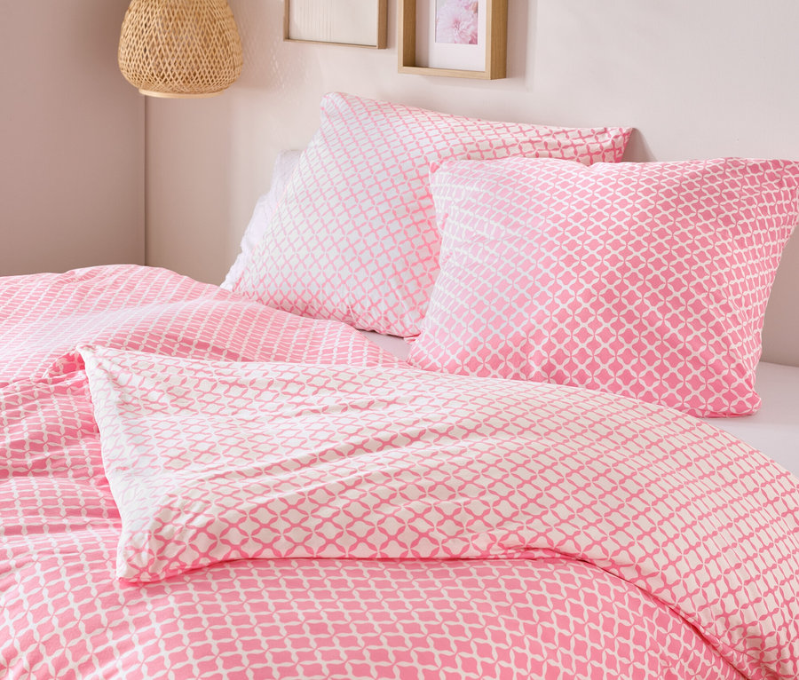 Nahaufnahme von einem Bett mit rosa-weisser Jersey-Bettwäsche, Normalgrösse und Übergrösse, mit zwei Kissen und einer Decke.