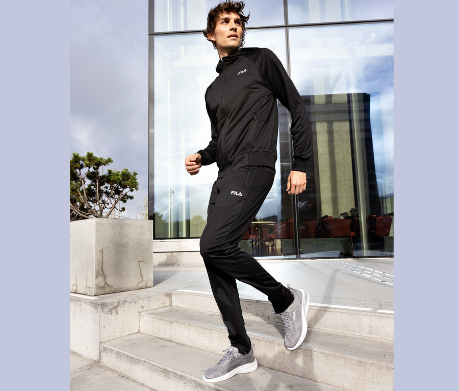 Mann in schwarzem Fila Trainingsanzug steigt eine Betontreppe hinunter, graue Fila Schuhe.