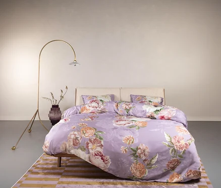Schlafzimmer mit Bettwäsche »Orianna« von Essenza in Normal- und Übergröße mit Blumenmuster, Lampe und Vase auf einem Teppich.