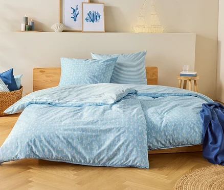 Ein blau-weißes Bett mit Ankermuster steht in einem Schlafzimmer. Auf dem Nachttisch steht ein Glas Wasser.