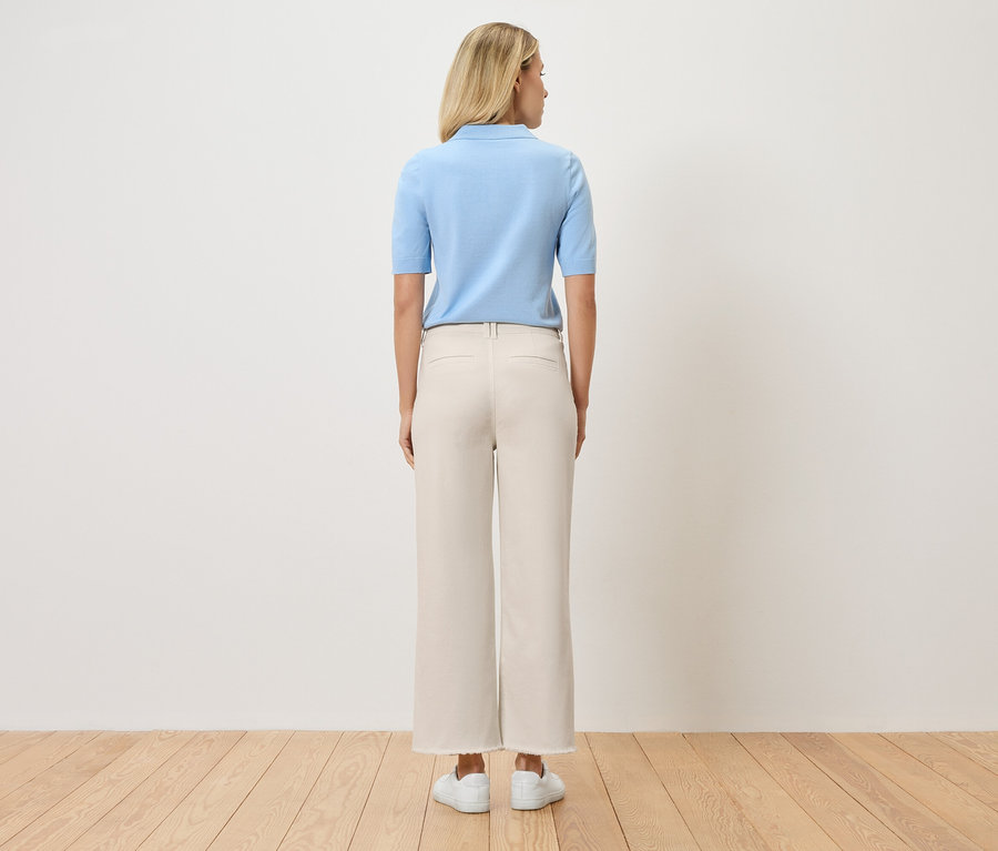 Rückansicht einer Frau mit blonden Haaren, die ein hellblaues Poloshirt, beigefarbene Hosen und weiße Schuhe trägt.