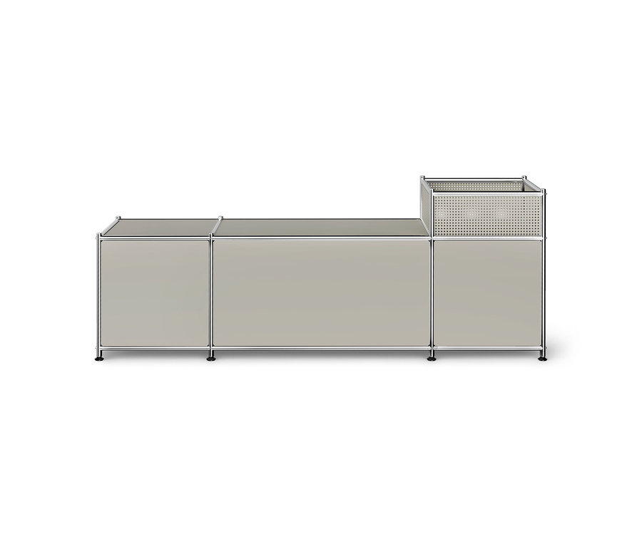 Hellgraues modulares Aufbewahrungsmöbel mit Chromrahmen, bestehend aus zwei niedrigeren Schränken und einem höheren rechten Element mit perforiertem Korbaufsatz, auf weißem Hintergrund.