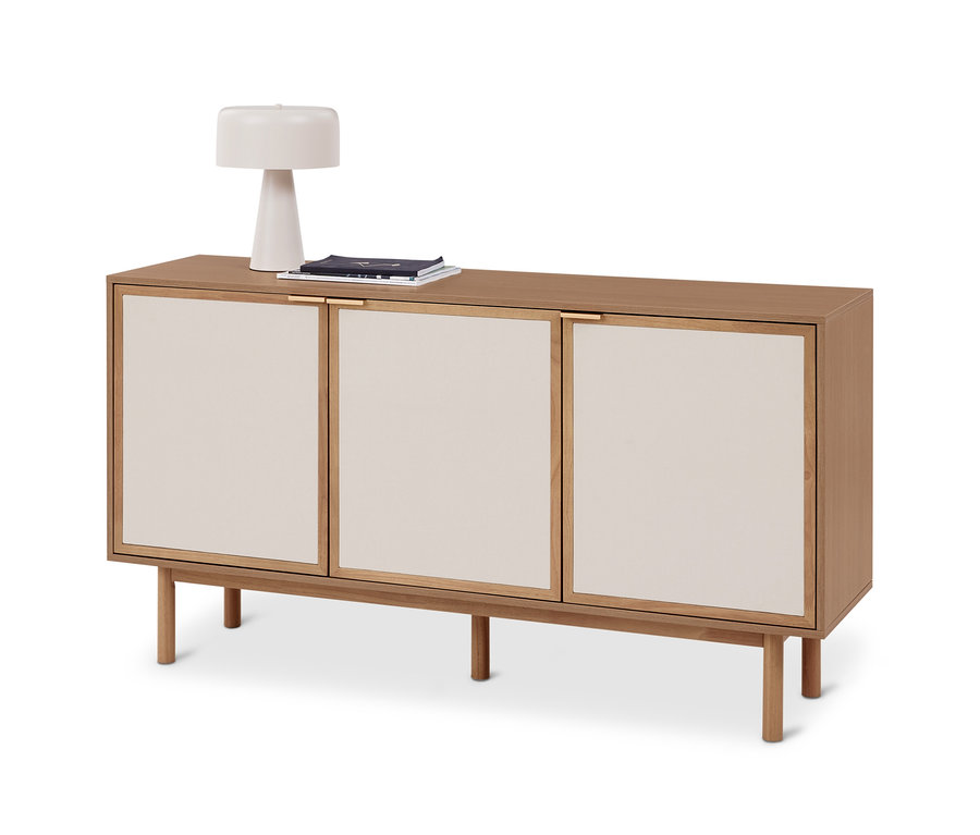 Helles Sideboard aus Holz mit drei cremefarbenen Türverkleidungen und vier Beinen. Darauf stehen eine weiße Lampe und ein Stapel Zeitschriften.