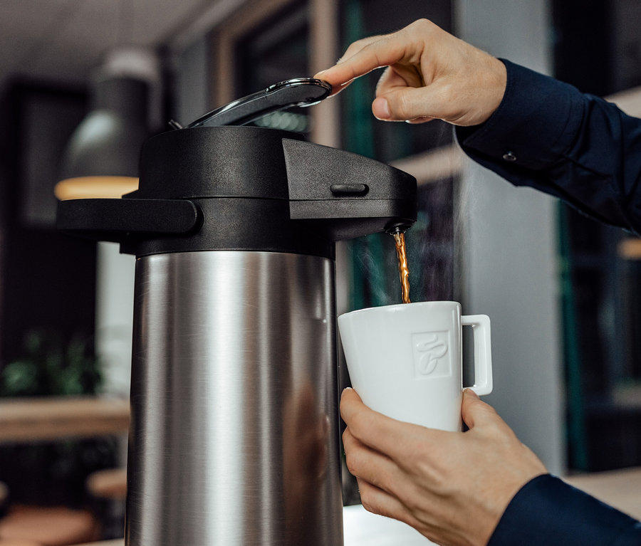 Person schüttet Kaffee aus einer Tchibo Businessline Pumpthermoskanne in eine weiße Tasse.