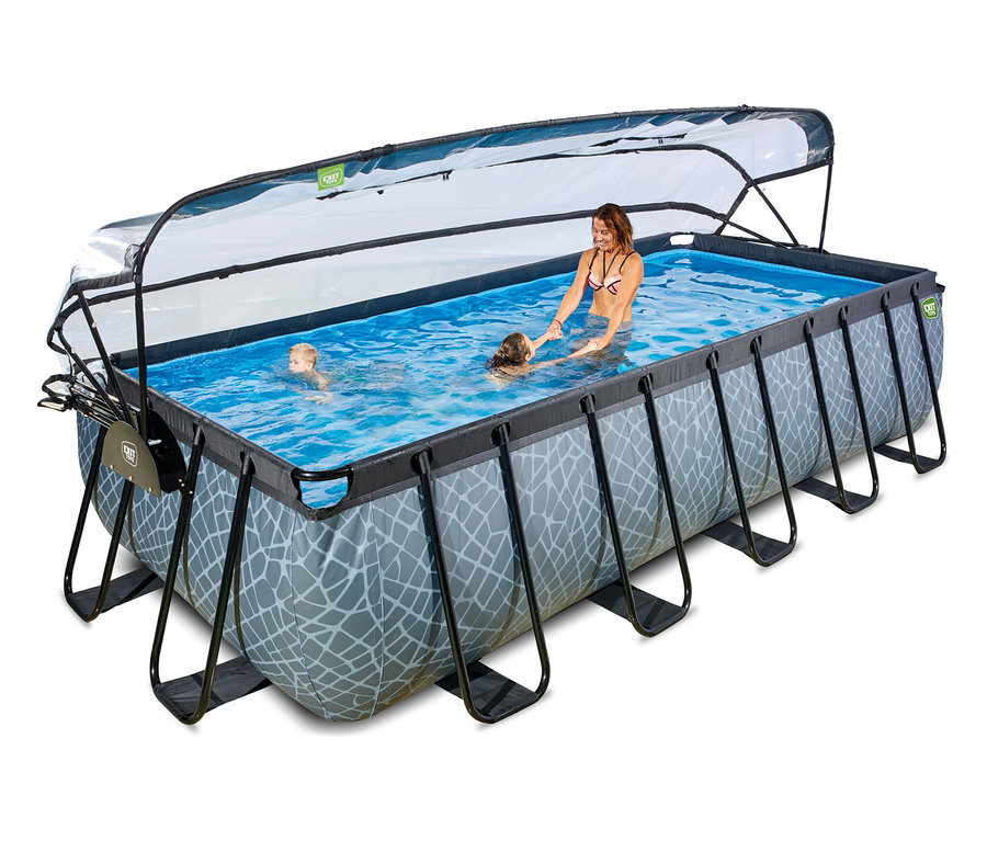 Eine Frau, ein Mädchen und ein Junge schwimmen in einem rechteckigen EXIT Pool-Set in Steinoptik. Der graue Pool hat eine teilweise geöffnete transparente Abdeckung.