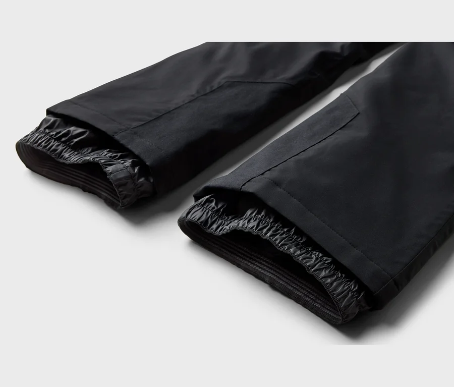 Zwei schwarze Hosenbeine mit elastischen Innenbündchen, wahrscheinlich Schneegamaschen, auf hellem Hintergrund.