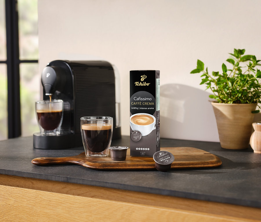 Kaffeemaschine bereitet Kaffee in ein Glas neben einer Packung Cafissimo Caffè Crema kräftig - 10 Kapseln zu.
