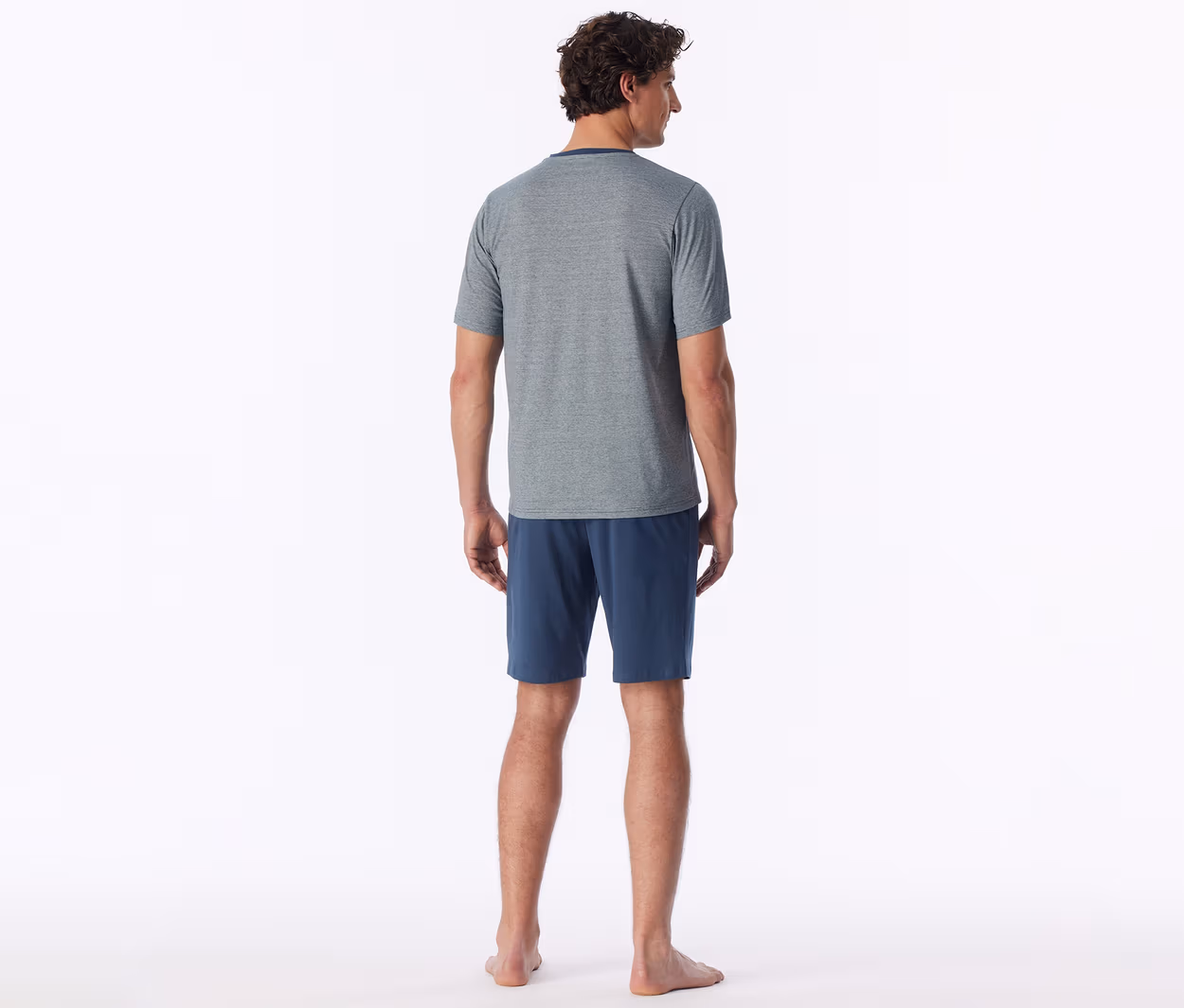 Mann von hinten, trägt ein graues T-Shirt und blaue Shorts, barfuß stehend.