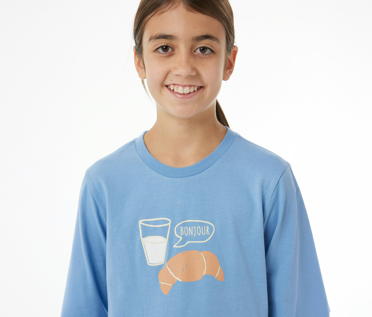 Lächelndes Mädchen trägt hellblaues SCHIESSER Kinder-Pyjama-Oberteil mit Milchglas-, Croissant- und „BONJOUR“-Aufdruck.