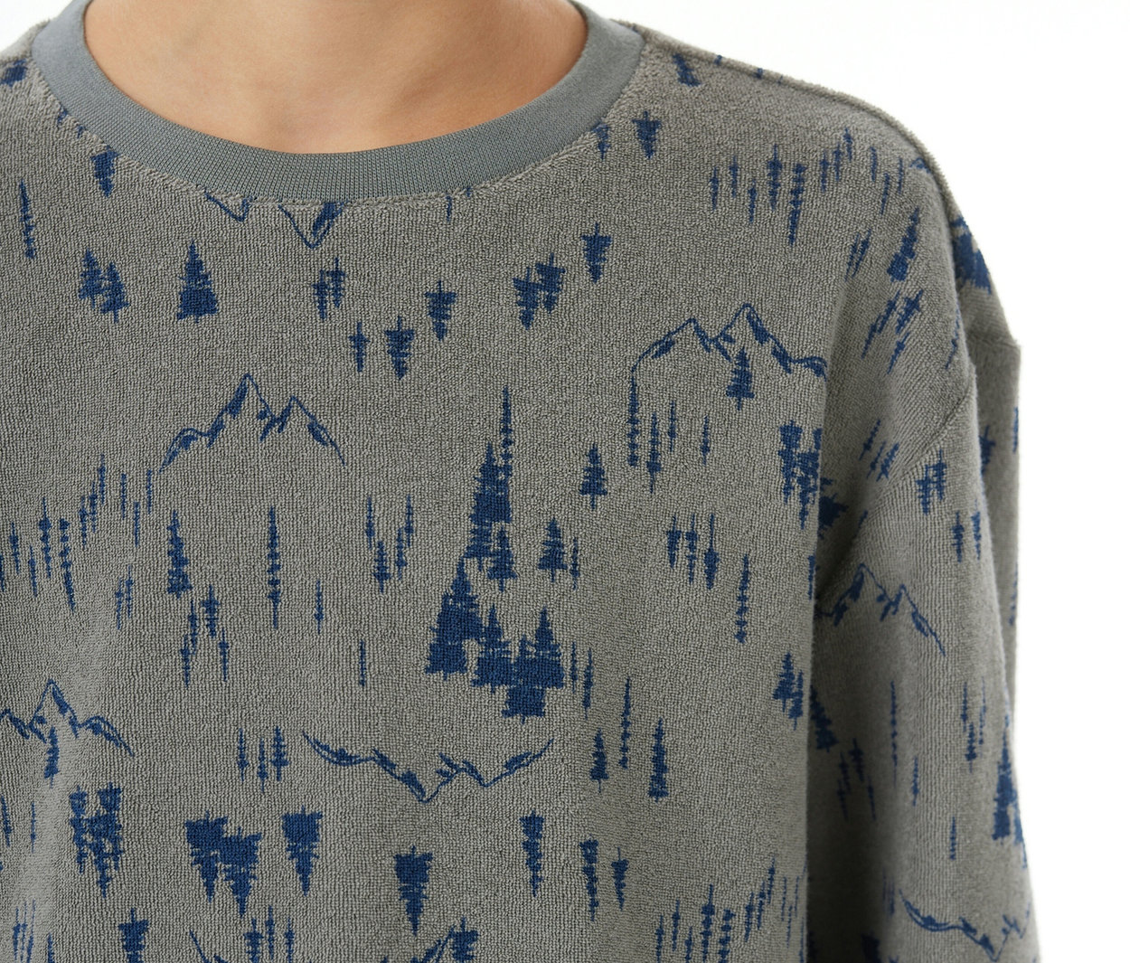 Kind in einem grauen SCHIESSER Kinder-Pyjama mit Bündchen, bedruckt mit blauem Berg- und Baummuster und grauem Rippkragen.
