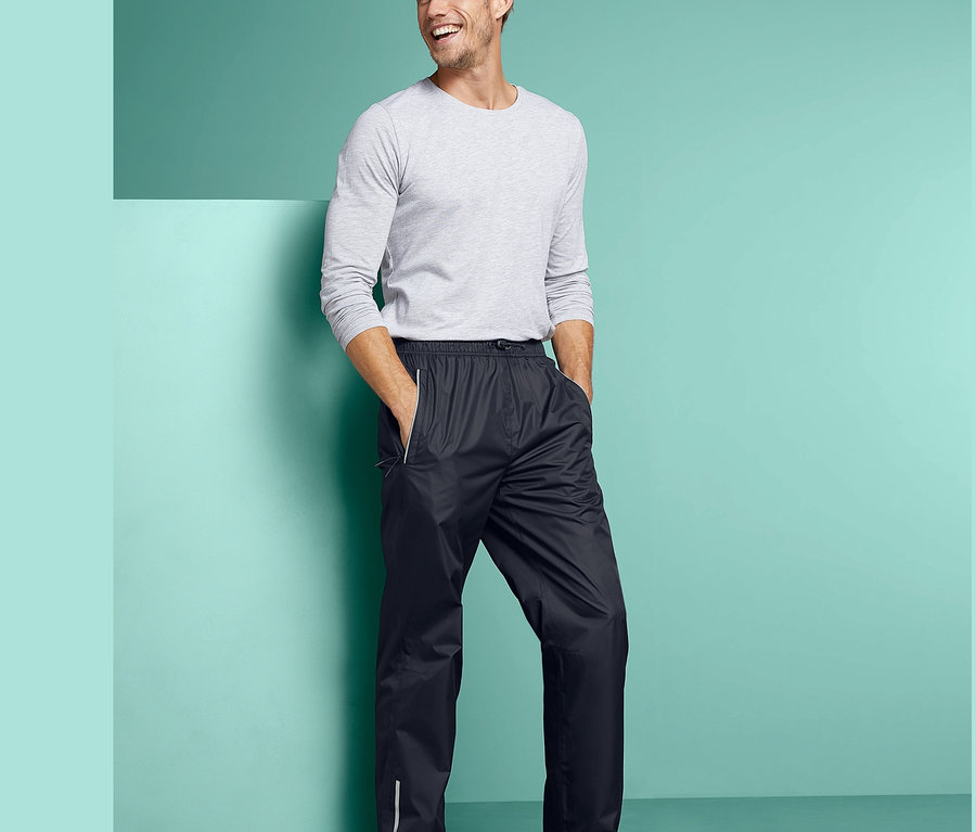 Mann steht mit Händen in den Taschen einer schwarzen Unisex-Regenhose.