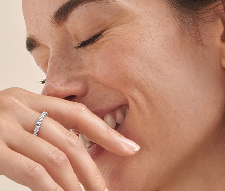 Lächelnde Frau mit geschlossenen Augen trägt eine silberne Kette mit Zirkonia, silberne Ohrstecker mit Zirkonia und zwei silberne Ringe Memoire mit Zirkonia.