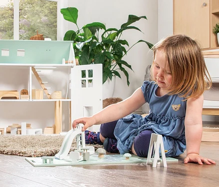 Mädchen spielt mit Pinolino Puppenhaus-Spielplatz-Set.