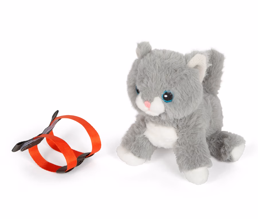 Eine graue small foot Stoffkatze mit Tasche und Pflege-Set liegt neben einer orangefarbenen Leine.