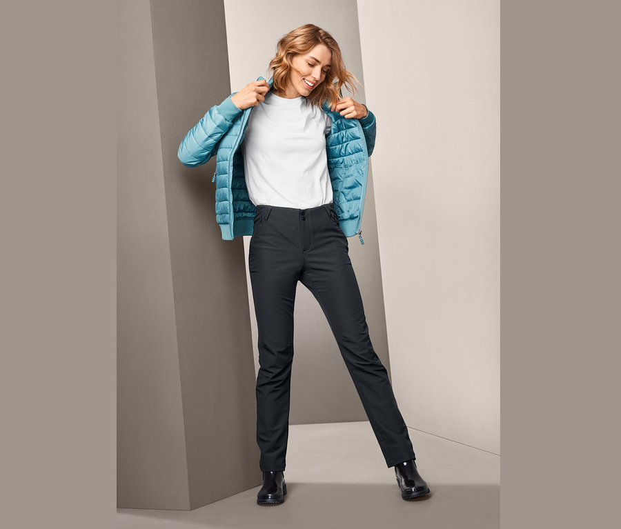 Frau zieht eine blaue Jacke an und trägt eine schwarze Softshellhose.