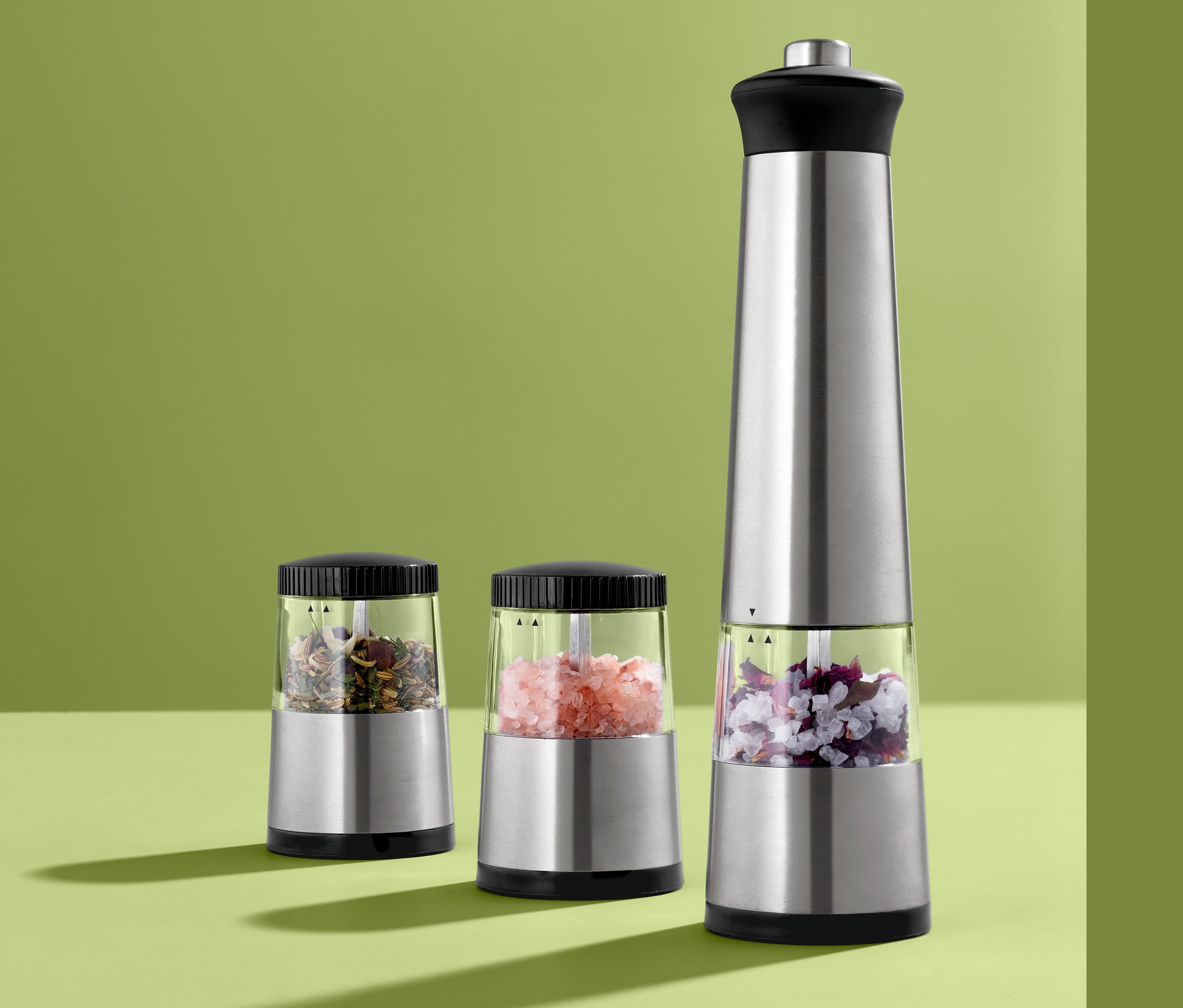 Drei elektrische Gewürzmühlen stehen auf einer grünen Oberfläche.