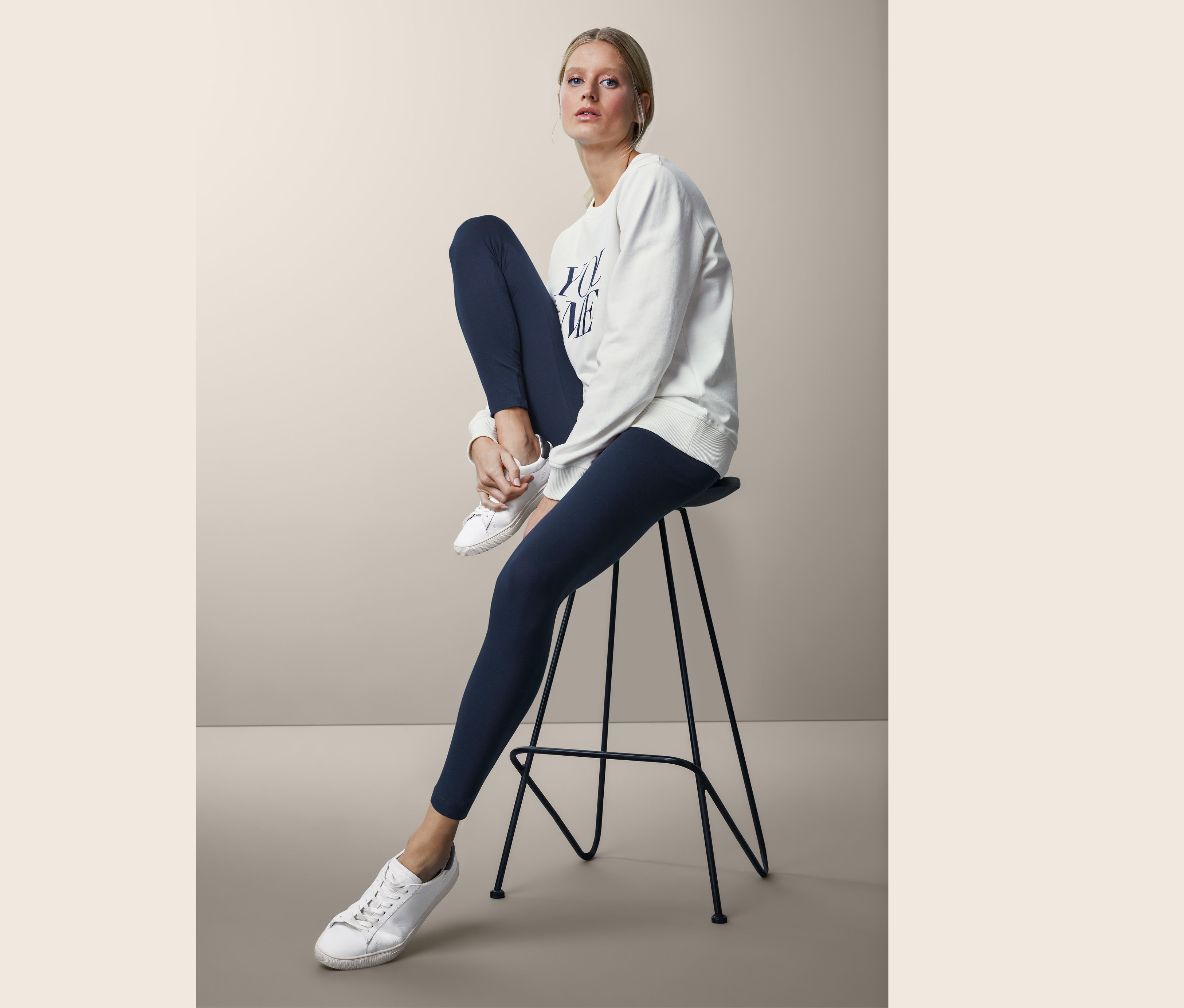 Frau sitzt auf einem Barhocker und trägt Leggings.